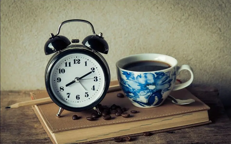 Coffee cup beside an alarm clock on a wooden surface